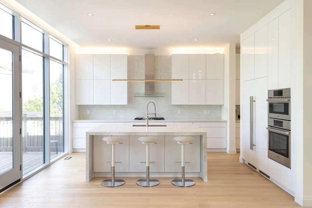 A modern white kitchen with stone countertops and appliances