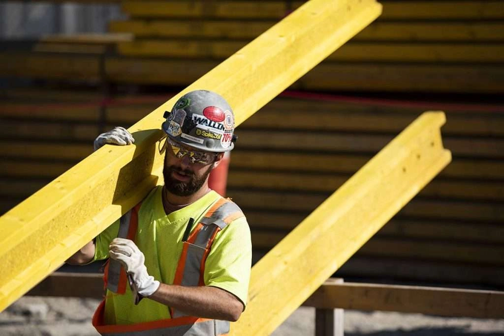 Construction worker carries metal beam