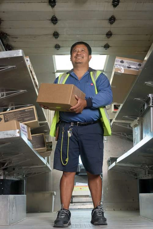 Mail worker holds box in back of truck smile