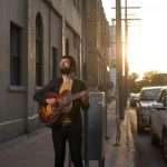 Musician stands on street corner holding guitar