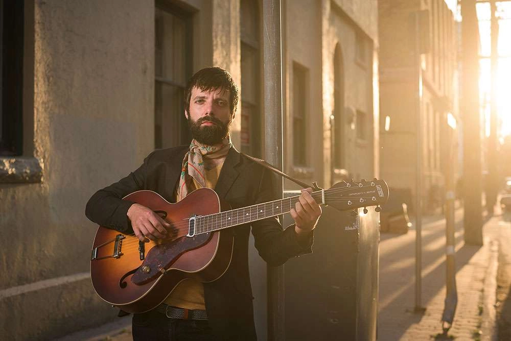 Musician in dramatic shot with sun holding acoustic guitar