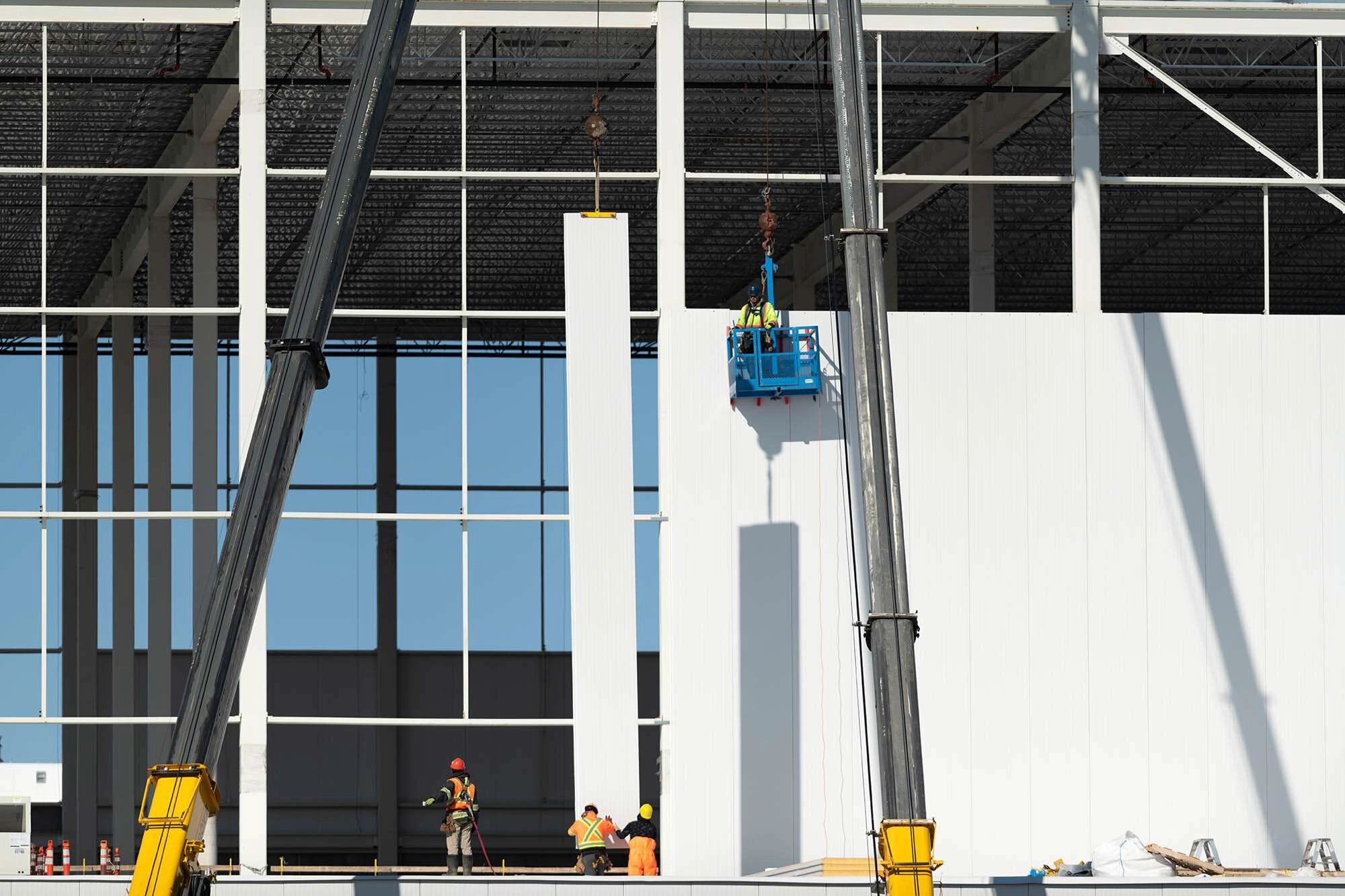 Workers install large panels by crane on a warehouse project. © robert lowdon