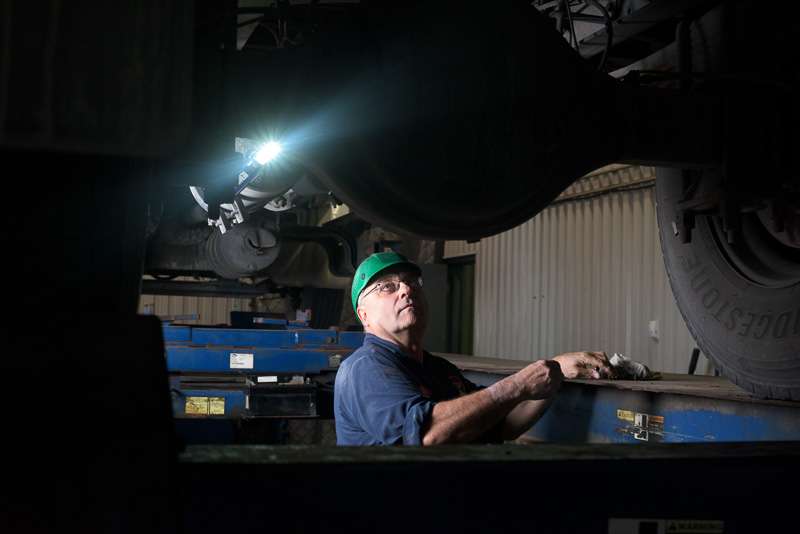 A mechanic works on a large postal truck on an industrial hoist.