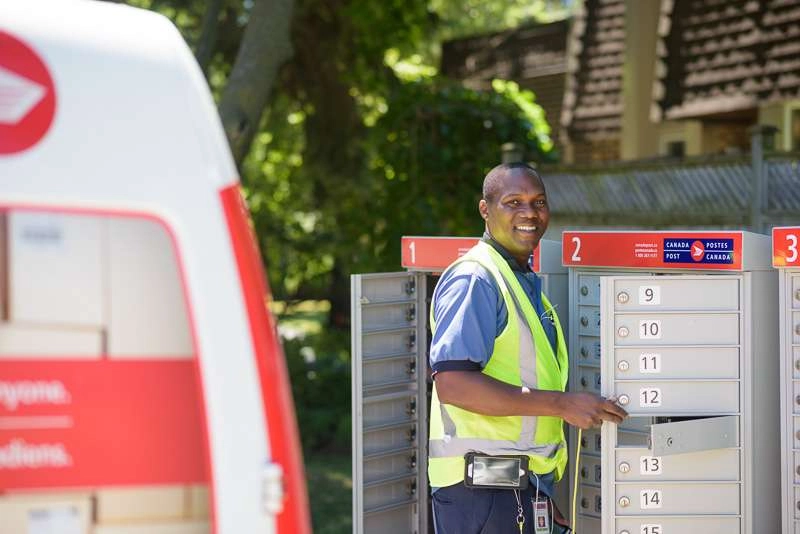 Mail carrier smiles at camera while loading mail boxes