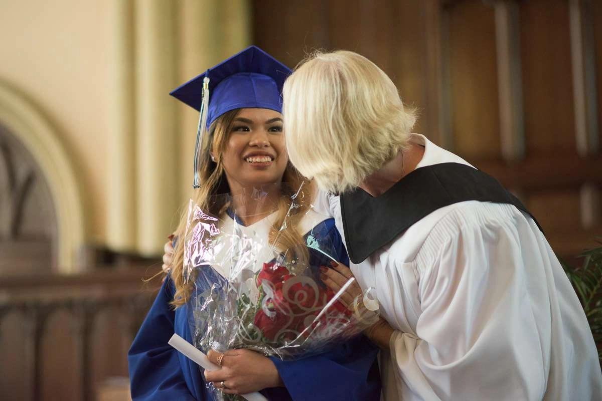 A smiling student is congratulated by her instructor. Both are dressed in academic regalia. A shallow depth of field is used to draw the eye to the student’s smiling face in this celebratory moment.