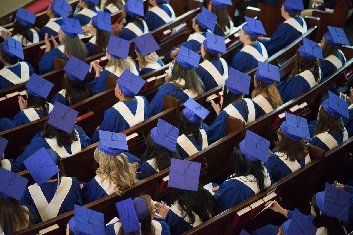 This overhead shot captures rows of seated graduands in blue caps and gowns. The downward angle emphasizes the number of students in the room and offers a visually interesting perspective.