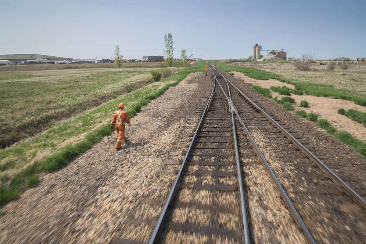 An employee walks on the gravel beside the train tracks towards a section of the track where a switch is located. This photograph is captured in motion, as can be identified by the blurring of the gravel and track in the foreground.