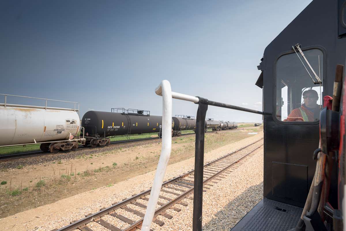 An employee sits aboard a train, looking out the window onto the rail yard. This image features a creative composition, positioning the employee in the right segment of the photograph.