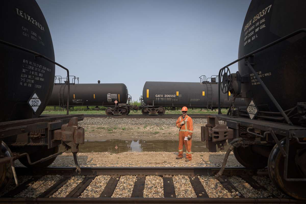 This image accentuates the colossal size of the tank cars by drawing a comparison to the size of an employee who stands beside to cars.