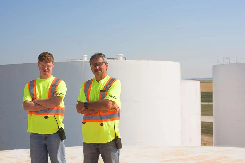Two people stand on top of large storage tank at an industrial facility