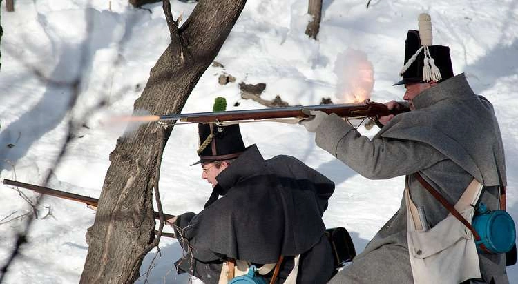 A man in period clothing fires a musket during a historic reenactment