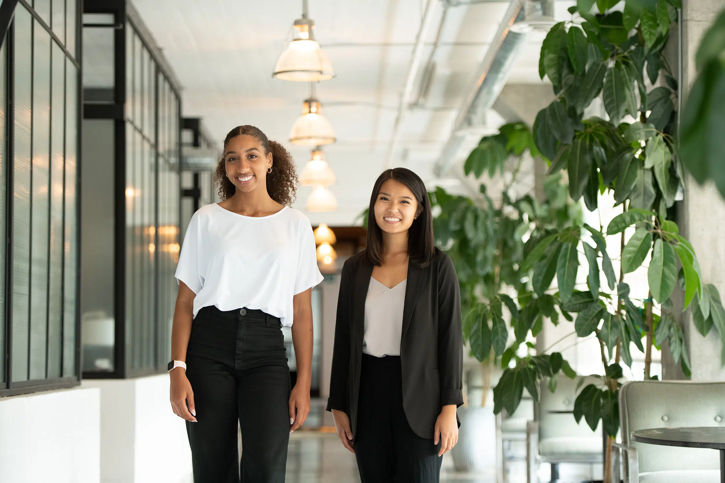 Two young female business professionals stop for a photo in a modern office.
