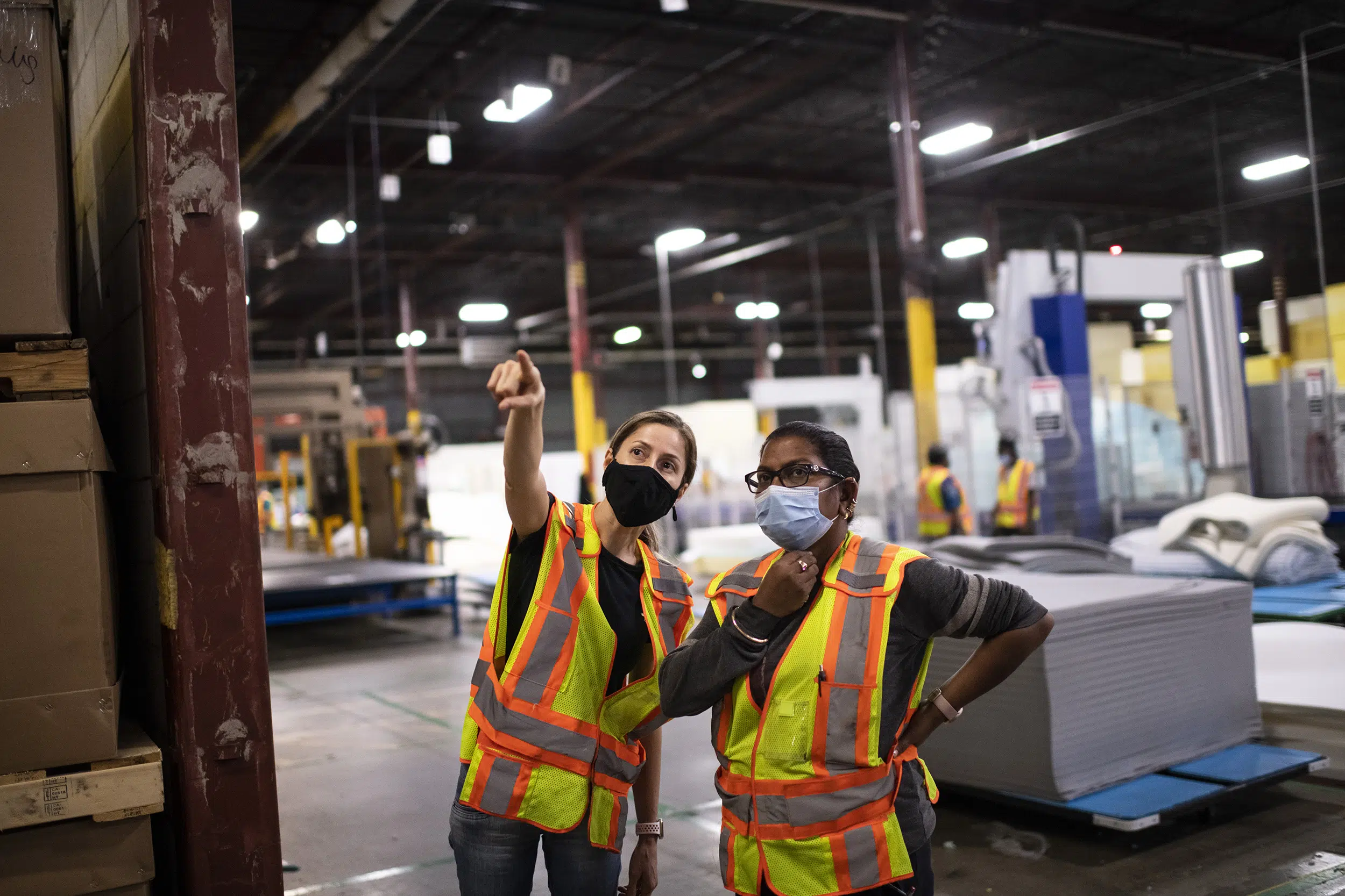 Two female workers in a manufacturing plant have a discussion.