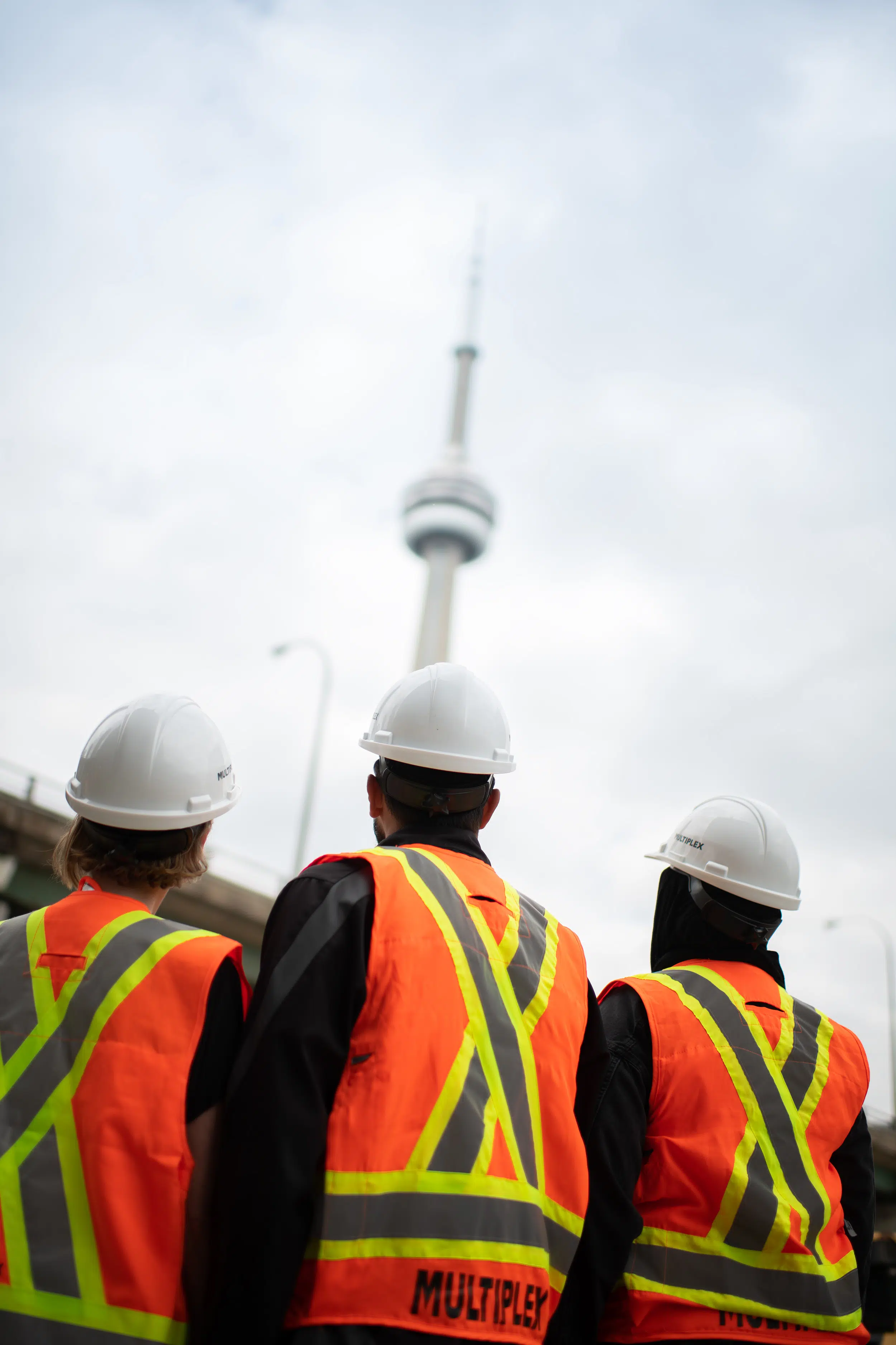 Three construction workers look up at the cn tower in toronto.