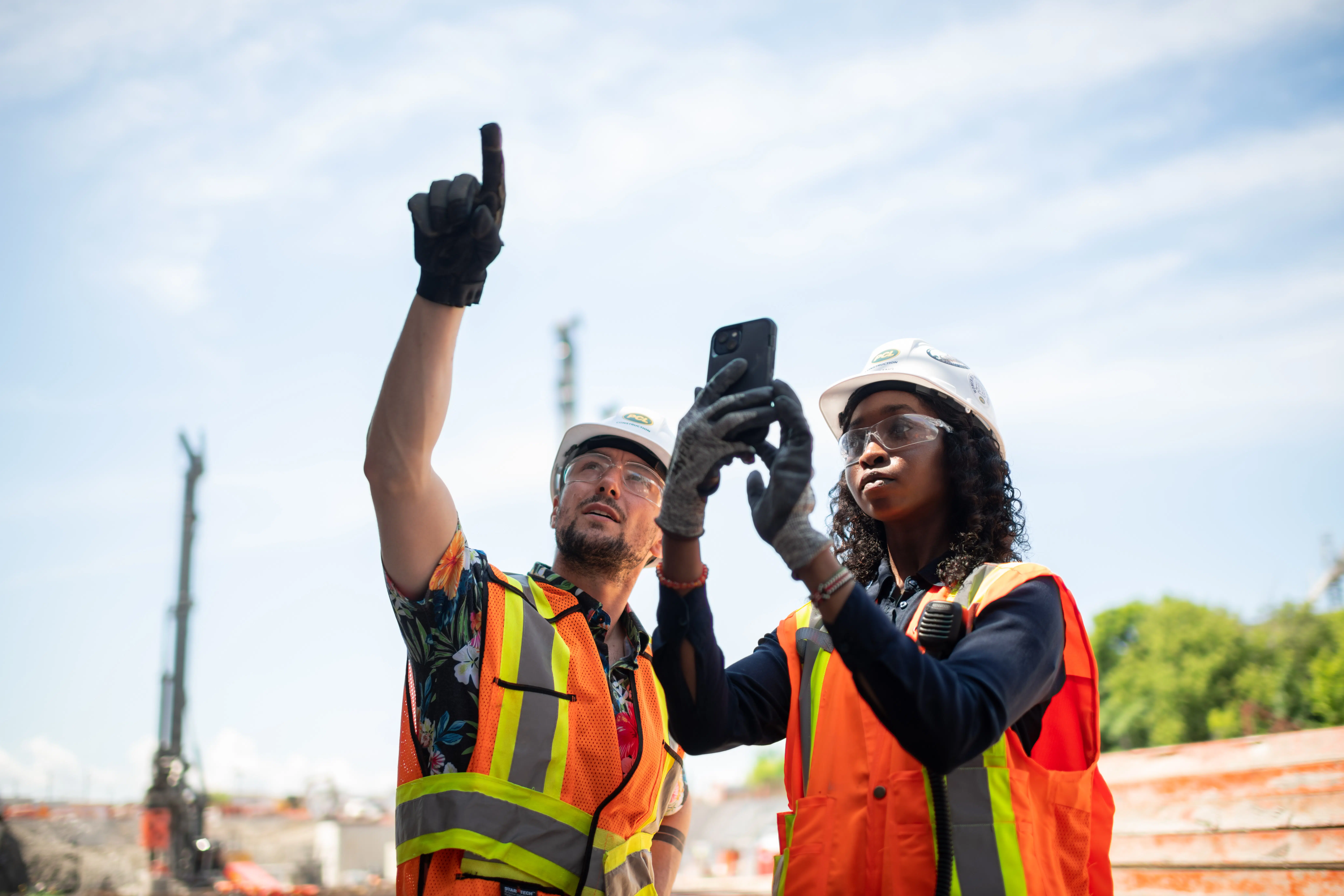 A female construction worker takes a picture while a male worker point s in the air.