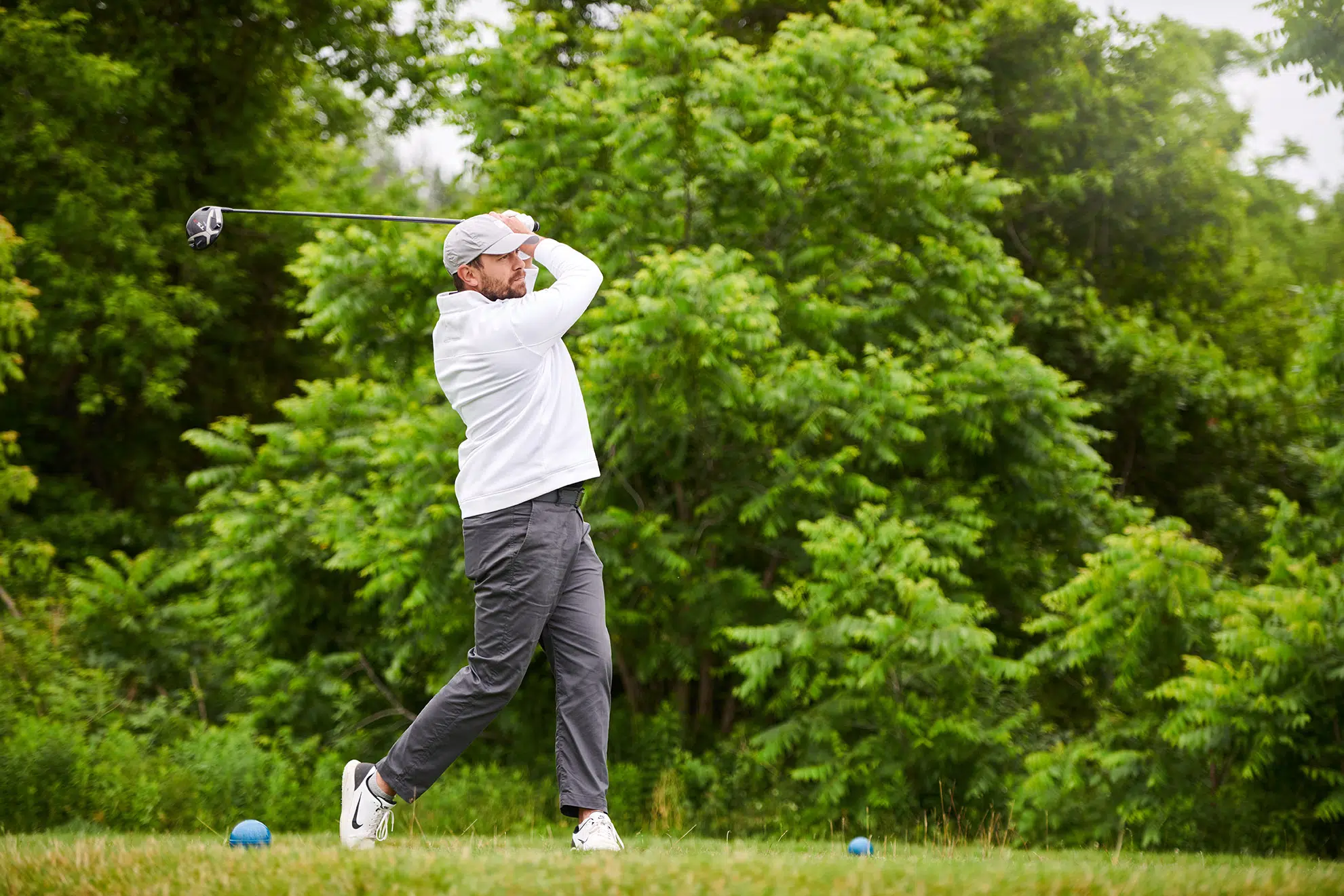 A golfer tees off with a forest background.