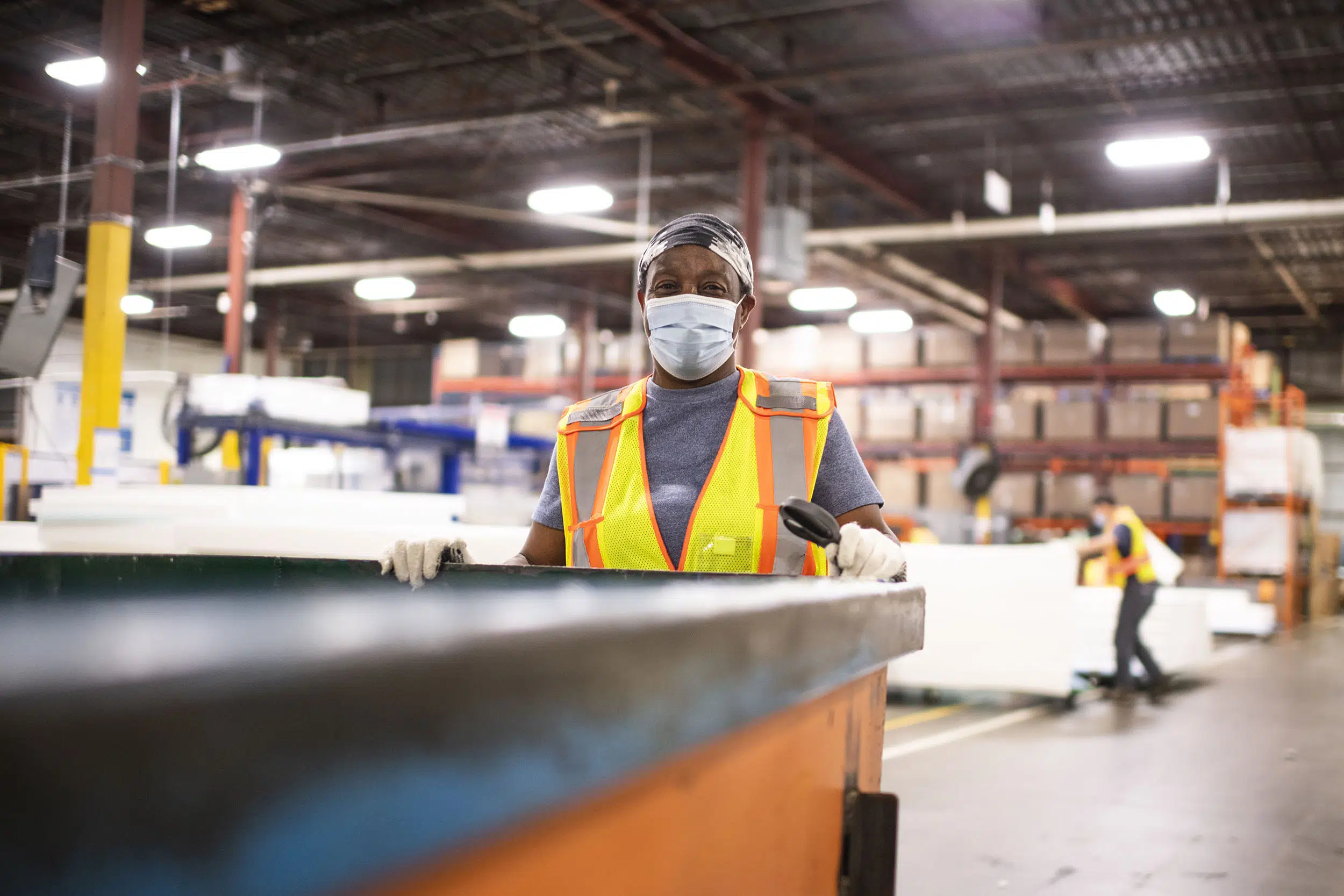 A worker moves a large cart across the factory floor, moving materials where they need to go.