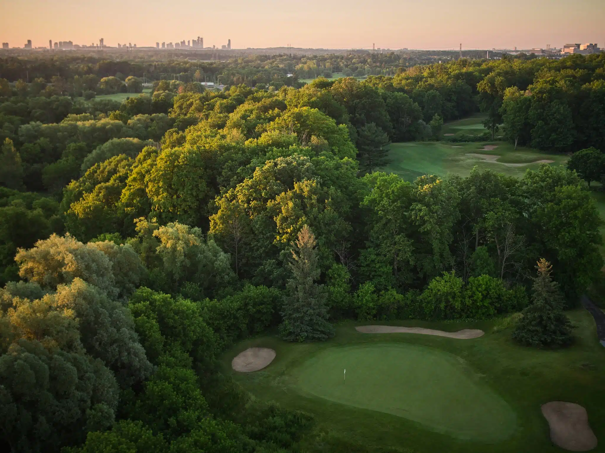Aerial image of golf course, with city scape far in the distance.