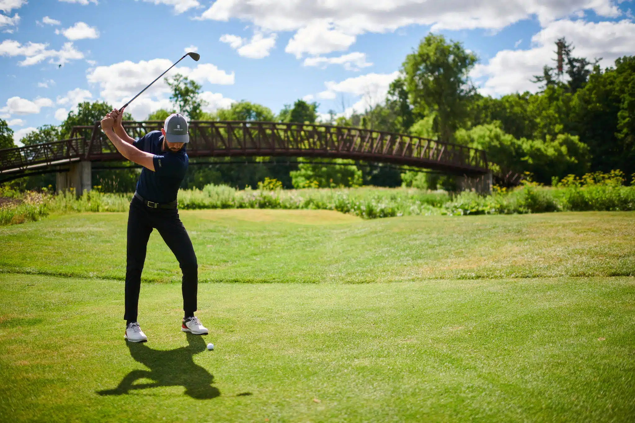 Golfer swinging club with signature bridge in background.