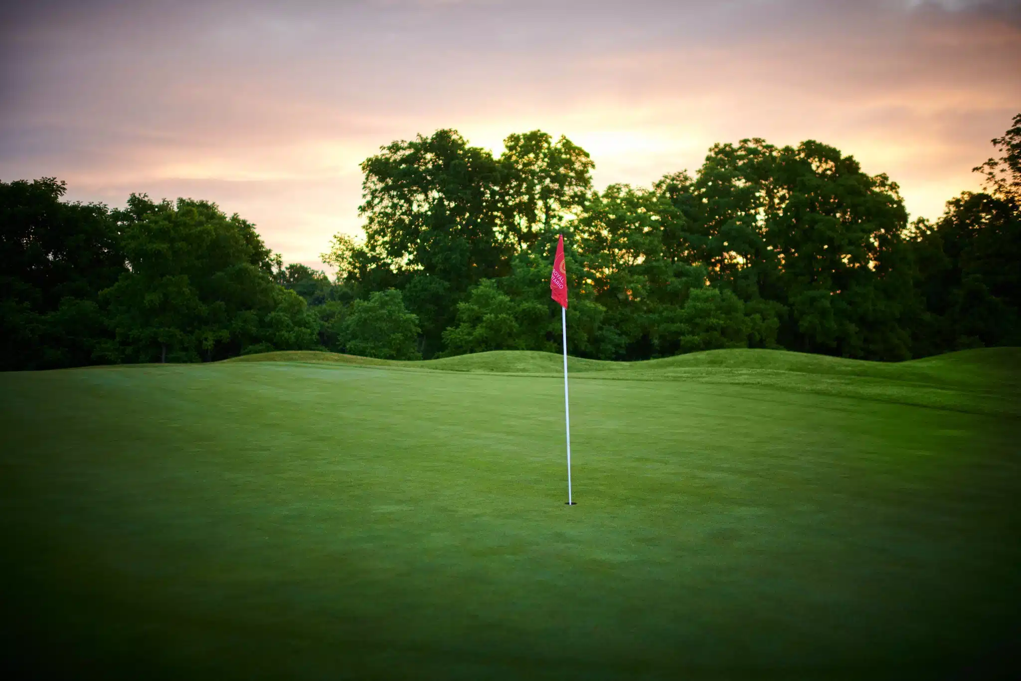 Light pink sunrise over the greens with red flag.