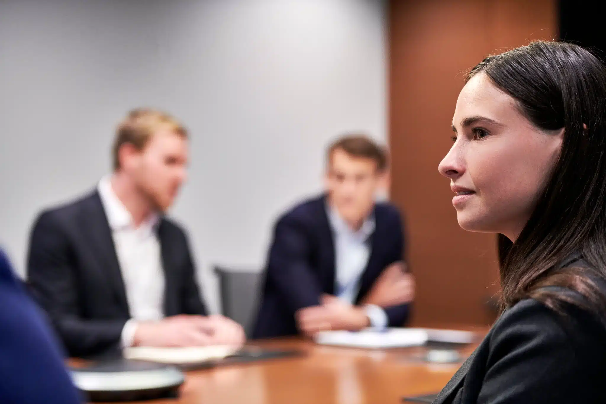 Female employee in focus, paying attention to presentation in a board room, with employees blurred in the background.